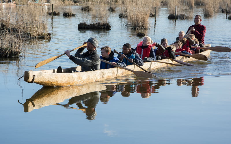 Kinderen en volwassenen peddelen in een boomstamkano door het water